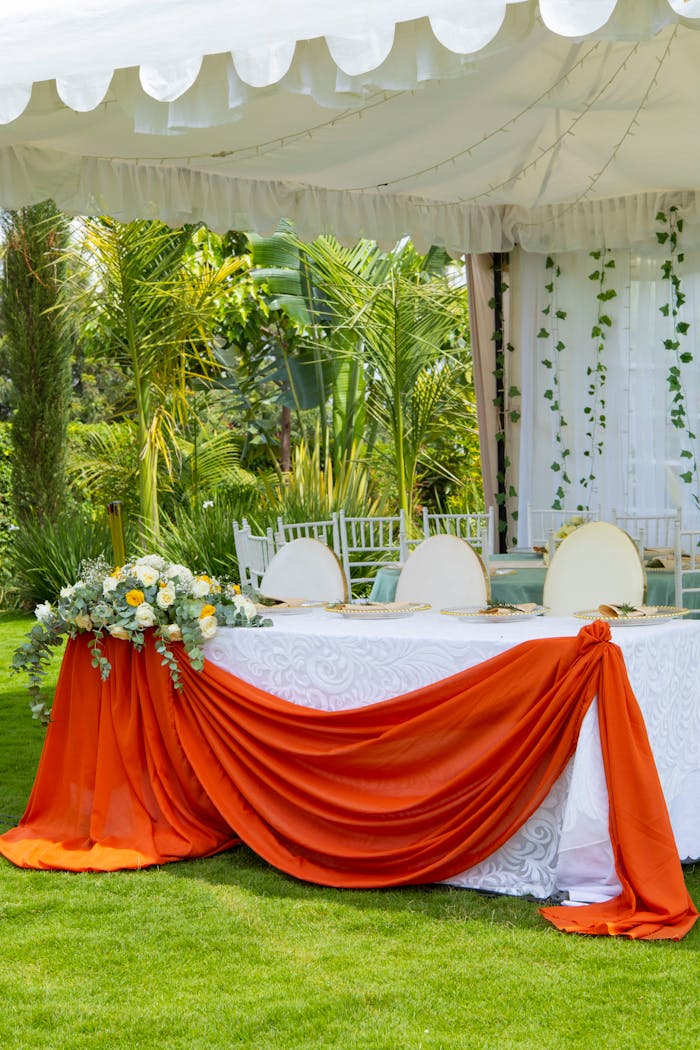 Beautifully decorated outdoor wedding table with orange drapery and green surroundings.